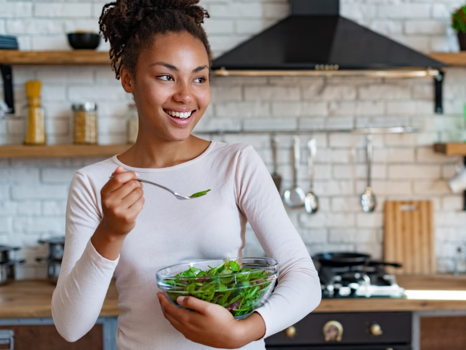 Mujer joven comiendo una ensalada en la cocina